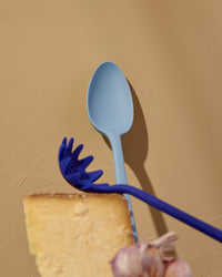 The Slate Mini Spoon on a cream background with the Spaghetti spoon in front of it. 